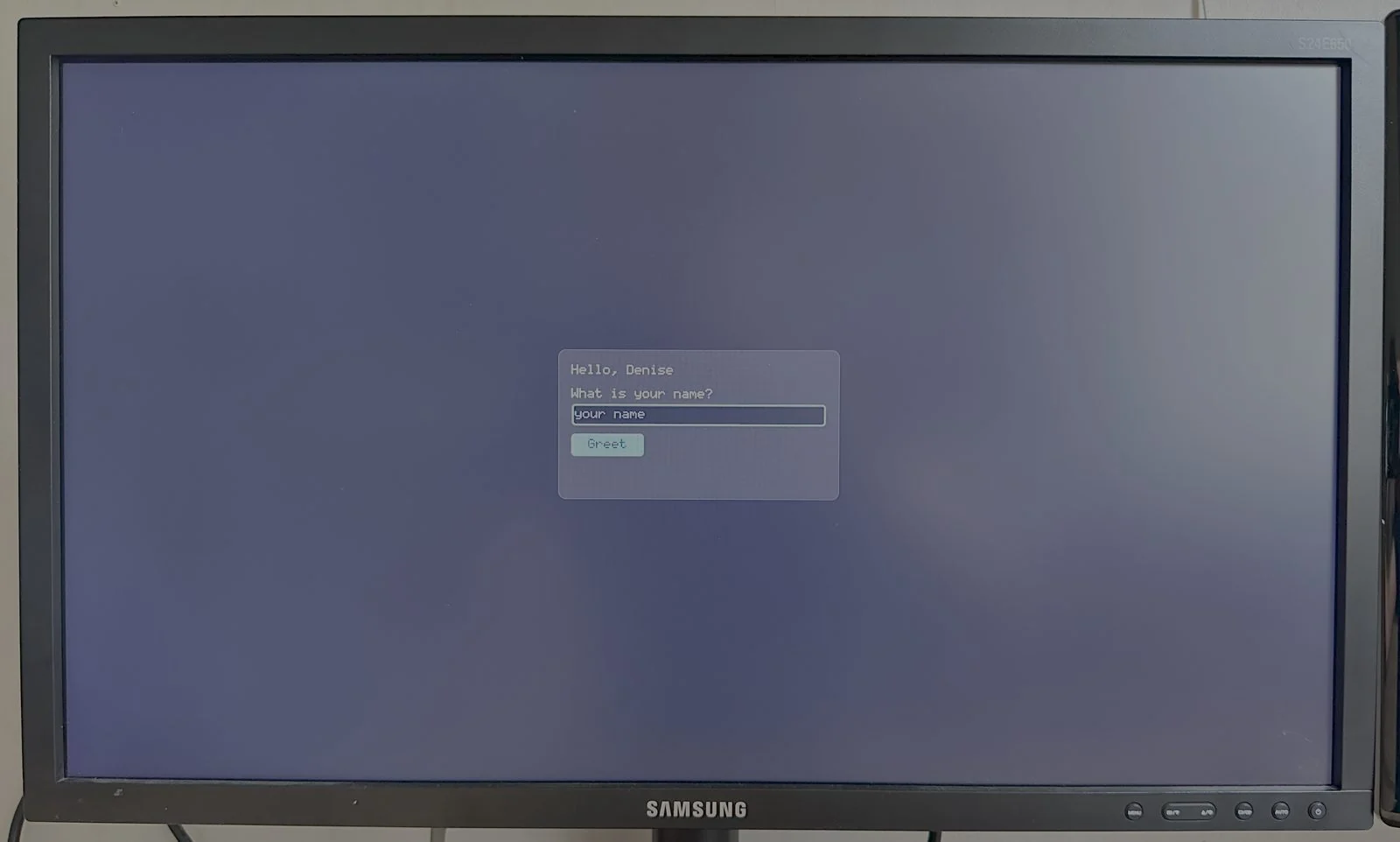 The hello example centred on the same monitor, drawn in the built-in bitmap font